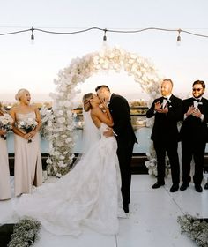 a bride and groom kissing in front of their wedding party on the roof of a building