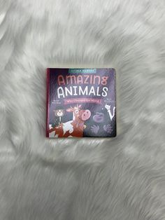 an animal book sitting on top of a white fur covered bedding with the title amazing animals