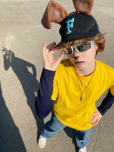 a young boy wearing sunglasses and a hat with ears on it's head, standing in an empty parking lot