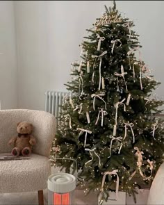 a small christmas tree is decorated with white ribbons and bows, while a teddy bear sits next to it