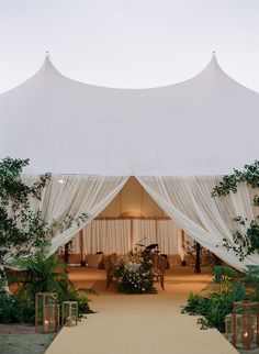 a large white tent set up for an outdoor wedding ceremony with greenery and candles