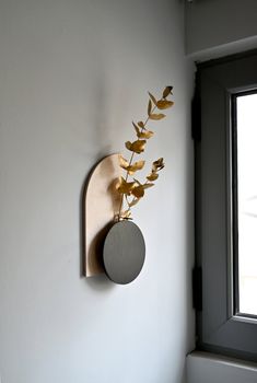 a wall mounted clock on the side of a white wall next to a vase with flowers in it