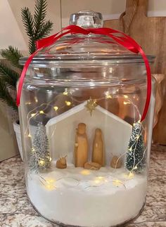 a christmas scene in a glass jar with lights and snow on the ground next to a tree