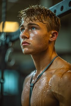 a shirtless man standing in front of a gym machine with water all over his body