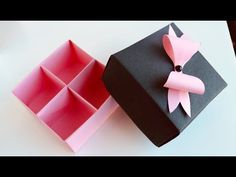 an origami box with a pink bow on the lid and another black box