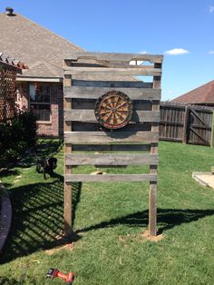 a wooden sign sitting on top of a lush green field next to a yard with a dart in it