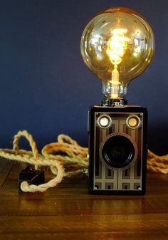 an old fashioned camera sitting on top of a wooden table next to a light bulb