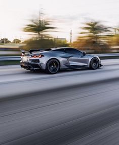 a silver sports car driving down the road with blurry trees in the back ground