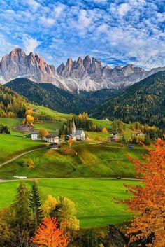 the mountains are covered in colorful trees and green grass, with houses on each side