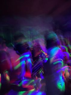 blurry photograph of people dancing in the dark with colored lights on them and one person holding a cell phone