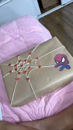 a gift wrapped in brown paper and decorated with spiderman stickers on top of a pink bed