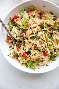 a white bowl filled with pasta salad on top of a marble counter next to a silver spoon