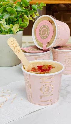 three pink ice cream cups sitting on top of a table next to a potted plant