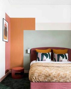 a bed with two pillows on top of it next to a wall painted in different colors