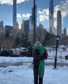 a woman is standing in the snow with her arms crossed and wearing a green scarf