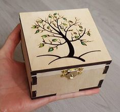 a hand holding a wooden box with a tree painted on it