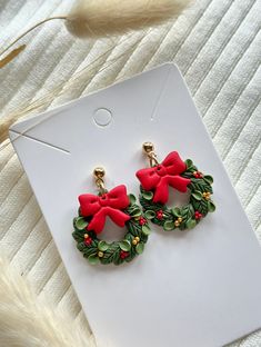 pair of christmas wreath earrings with red bows and holly leaves on white carded background