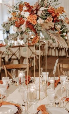 a tall centerpiece with orange flowers and greenery is on top of a table