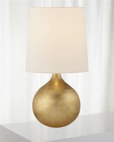 a gold table lamp with a white shade on the top and bottom part of it