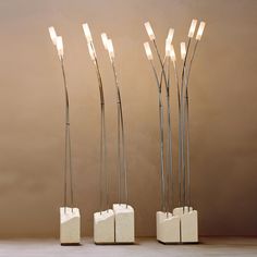 four tall metal sculptures with lights in them on a table next to a brown wall