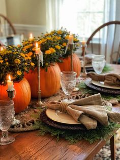 a wooden table topped with plates covered in pumpkins and greenery next to candles