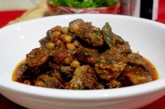 a white bowl filled with meat and beans on top of a table next to a red cloth