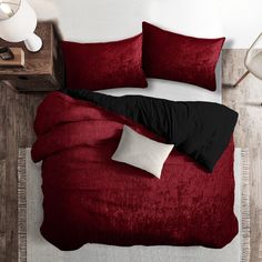 a bed with red and black comforters in a room next to a lamp on a table