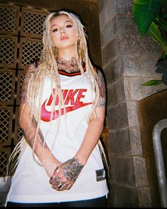 a woman with blonde hair and tattoos standing in front of a brick wall