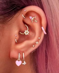 a woman with pink hair wearing three different ear piercings and one has a heart