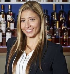 a woman standing in front of a bar with bottles on the wall behind her and smiling