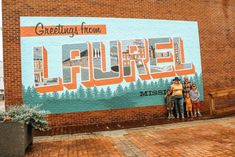 two people are standing in front of a mural on the side of a building that says laurel