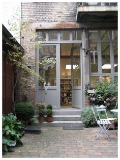 an outside view of a building with potted plants on the sidewalk and chairs in front