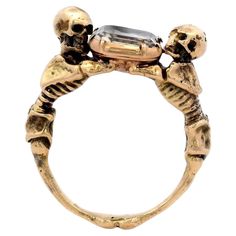 This Georgian style ring features two skeletons looking above and below while embracing a stuart crystal and is made from 18 karat gold. This statement ring features a colorless rock crystal, elevated by two intricately detailed skeletons. The skeletal figures embrace the stone together, creating an enchanting focal point. The band, also in yellow gold, echoes the skeletal design with refined features. A remarkable fusion of elegant, gloomy, and whimsical design. A bold choice for those who appreciate exceptional creativity in their jewelry. Signage: None but Size: 6.75 Condition: Excellent , with minimal signs of wear Year: Circa 1960 Weight: 10.0 grams total Please feel free to reach out with any questions, comments, or concerns. We will get back to you as soon as possible.  100% Money B Two Skeletons, Accessory Inspo, Double Band Rings, Vintage Tiffany, Whimsical Design, Crystal Skull, Skull Ring, Cartier Ring, Rock Crystal