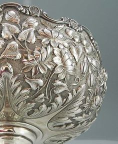 an ornate silver bowl with flowers and leaves on it