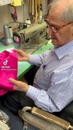 an older man sitting in front of a sewing machine with a pink bag on his lap