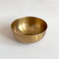 a gold colored bowl sitting on top of a white tableclothed surface with no one in it