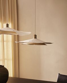 three lamps hanging from the ceiling above a dining room table with chairs and a vase