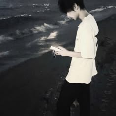 a young man standing on the beach looking at his cell phone while holding something in his hand