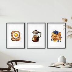 three framed pictures hanging on the wall above a dining room table with a coffee pot, pancakes and an egg