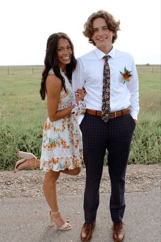 a young man and woman standing next to each other in front of an open field