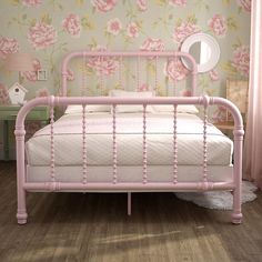 a pink metal bed frame in a bedroom with floral wallpaper and wooden flooring