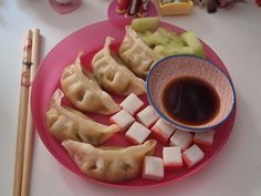 a pink plate topped with dumplings next to chopsticks and a bowl of sauce