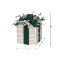 a green and white gift box with ribbon on it's side, sitting next to a ruler