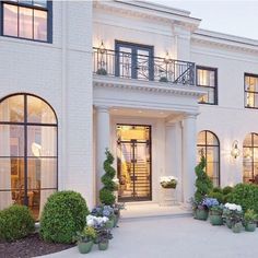 a large white house with lots of windows and potted plants in the front yard