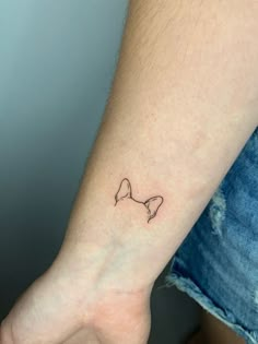 a small bow tattoo on the left inner wrist is shown in black ink, with an outline of a dog's head