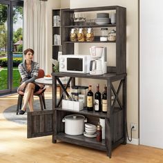 a woman sitting at a table in front of a microwave and other kitchen items on shelves