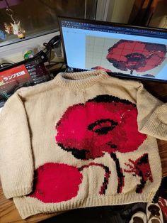 a sweater with red flowers on it next to a laptop computer