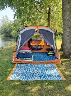 an orange tent is set up in the grass near a tree and some blue rugs