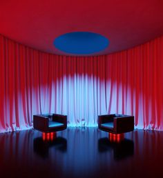 two chairs sitting in front of a red and blue curtained room with round lights