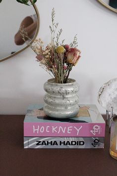 a stack of books sitting on top of a table next to a vase filled with flowers